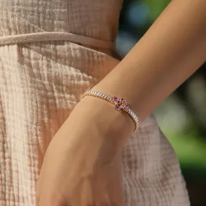 Detail of 18K gold tennis bracelet with white zircon and pink cross on model's wrist