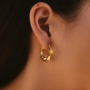 Primo piano di un orecchino a cerchio dorato intrecciato con texture a spirale su modella