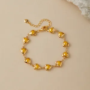 Close-up of golden heart-shaped bracelet with amber-colored resin inlays and lobster clasp