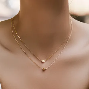 Detailed close-up of a layered gold necklace featuring an oval pendant and metal bead