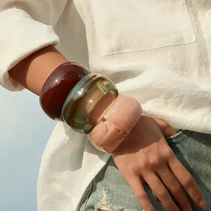 Three wide bohemian acrylic bangles in amber, green and cream on a model's wrist