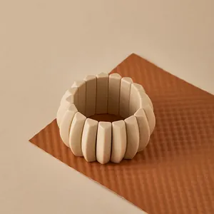 Detalle de una pulsera elástica ancha de resina beige con eslabones geométricos mates