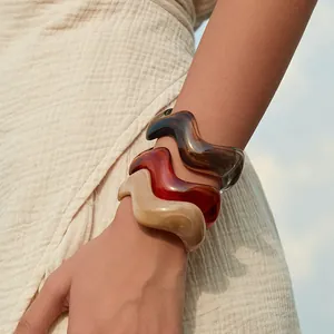 Detailed view of wave-shaped acrylic bangles in amber, tortoiseshell, and marble patterns