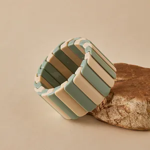 Détail du bracelet élastique en acrylique mat vert sauge et marron posé sur une pierre