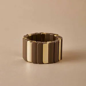 Détail d'un large bracelet élastique avec des pièces rectangulaires marron foncé et dorées