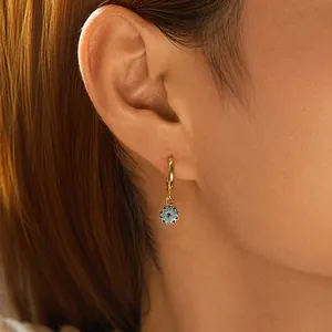 Nahaufnahme von 18K vergoldetem Blumenohrring mit blauem Steinanhänger am Modell