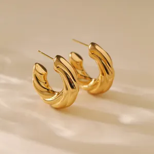 Close-up of golden irregular C-shaped hoop earrings with spiral textured pattern