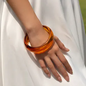 Macro detail of amber acrylic chunky bangle with textured swirl resin finish on wrist