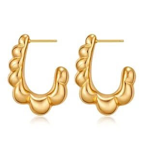 Detail of high-polished gold chunky C-shaped hoop earrings with wavy edge design