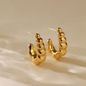 Detail of 18K gold-plated C-shape croissant ribbed stud earrings on a warm background
