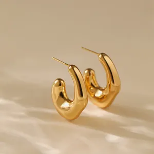 Close-up of golden chunky C-shaped hoop earrings with a molten mirror finish on beige fabric