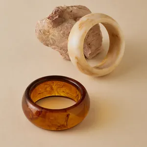 Detail of wide acrylic bangles in marble white and translucent amber on a stone background
