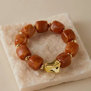 Detailed macro view of amber marble resin square beads and gold irregular charm bracelet