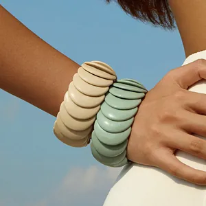 Close-up of chunky stacked resin bracelets in cream and sage green against a clear sky