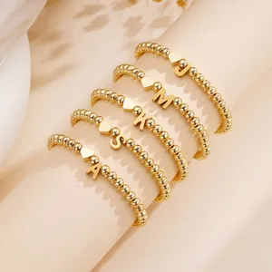 Gold beaded heart bracelet with personalized letter charms shown on an elegant scroll