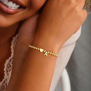 Detail of gold beaded bracelet with a polished heart charm and letter A pendant