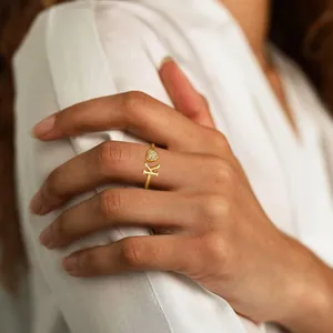 Golden open ring with letter K and zircon-set heart charm on a model's hand