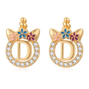 Détail de boucles d'oreilles licorne dorées lettre D avec zircons et fleurs colorées