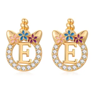 Détail de boucles d'oreilles licorne dorées avec lettre E, zircone et fleurs en émail