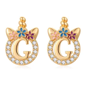 Détail de boucles d'oreilles licorne lettre G dorées avec fleurs émaillées et zircons brillants