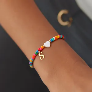 Colorful beaded bracelet with white heart charm and golden letter S pendant on model's wrist