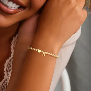 Close-up of a gold beaded bracelet with heart and letter H charms on a woman's wrist