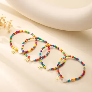 Colorful beaded bracelet set with gold initial charms and white heart beads on a warm base