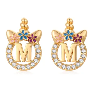 Détail des boucles d'oreilles lettre M dorées avec fleurs en émail coloré et zircons