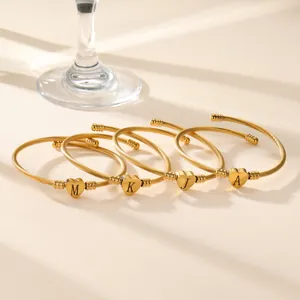 Four gold twisted wire bracelets with heart letter charms M K J A in warm lighting