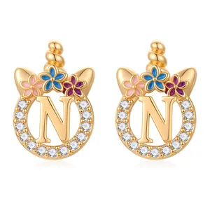 Détail de boucles d'oreilles licorne dorées avec lettre N, fleurs en émail et oxydes de zirconium