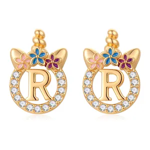 Détail de boucles d'oreilles lettre R dorées avec corne de licorne et zircons