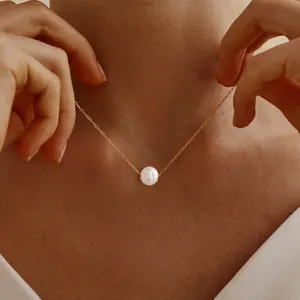 Eleganter einzelner weißer Perlenanhänger an einer dünnen Goldkette am Hals des Models