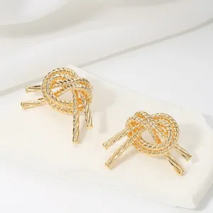 Detailed close-up of gold twisted rope knot stud earrings on white stone display