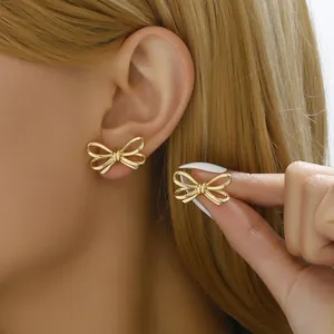Close-up of elegant gold ribbon bow earrings worn by a model with golden hair