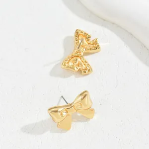 Elegant gold bow earrings with high-polish finish on a minimalist textured surface