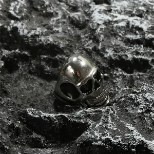 Macro view of polished stainless steel skull ring on dark volcanic rock background