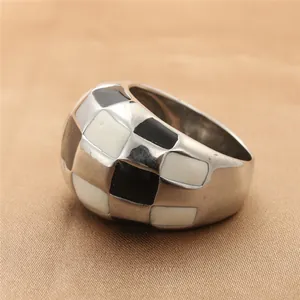 Close-up of a wide stainless steel ring with black and white checkerboard enamel design