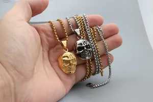 Detailed view of gold and silver skull pendants with box chains held in hand