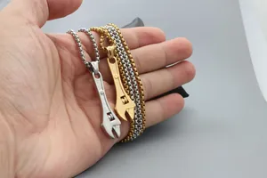 Detail of mini adjustable wrench pendant necklaces in gold and silver held by hand
