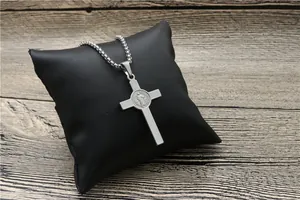 Detail of silver St. Benedict cross pendant with religious medal on a black leather cushion