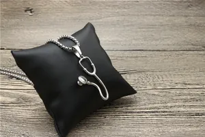 Detailed view of a silver stethoscope pendant necklace on a black textured cushion