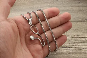 Detail of silver stethoscope pendant with box chain held by hand over wooden surface