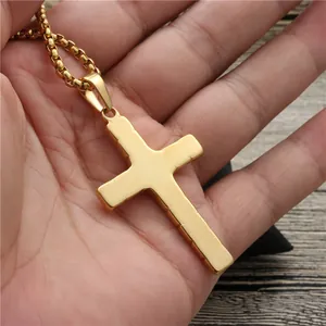 Polished gold cross pendant necklace with box chain held in hand for size comparison