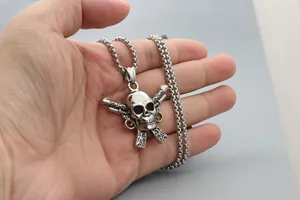Primer plano del colgante punk de acero con calavera y dos pistolas en una cadena box