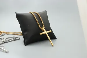Detail of gold cross pendant with bamboo texture on box chain over black leather pillow