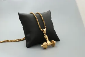 Macro shot of gold dumbbell necklace with muscular arm pendant on a black cushion
