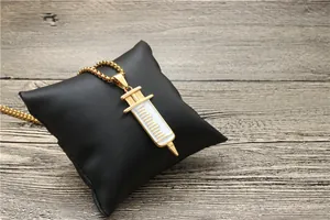 Detailed view of a gold syringe pendant necklace with white enamel on a leather cushion