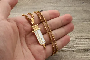 Close-up of gold syringe pendant with white enamel detail on a delicate chain