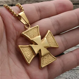 Golden iron cross pendant necklace with textured surface held in hand on wood