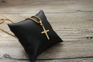 Detail einer goldenen Kreuzkette auf schwarzem Satinkissen mit Box-Kette